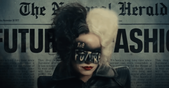 A queer Halloween costume for 2023. The image shows Emma Stone as Cruella, with a newspaper background. The photo is from the shoulders up, with a woman who has white and black hair, bright red lipstick and black smudges on her face and with writing that reads – the future.