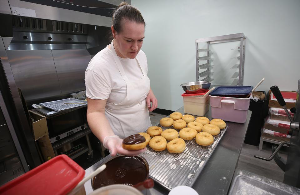 Destination Donuts general manager Holly Colley dips doughnuts into chocolate during the opening day at the new Clintonville location April 7.