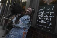 Taylor Swift fan Brodie MacArthur from east London poses with a friend's dog next to a sign featuring Taylor Swift lyrics outside The Black Dog pub in Vauxhall, London, Saturday, May 4, 2024. As Taylor Swift prepares to launch the Europe leg of her blockbuster Eras tour, thousands of her fans from the U.S. and Canada are following her across the pond. (AP Photo/Alastair Grant)