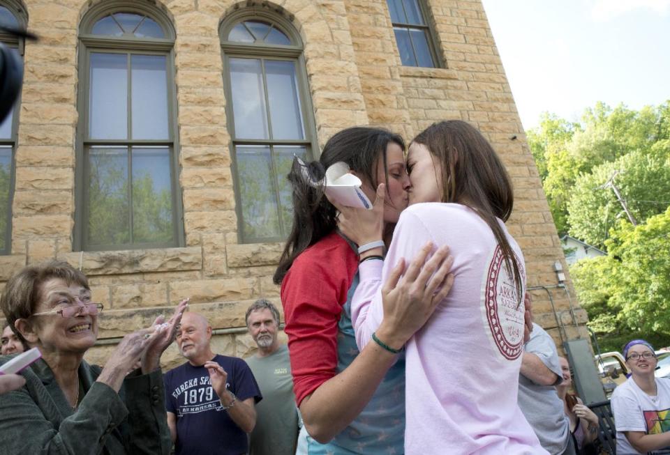 Jennifer Rambo, right, of Fort Smith, Ark., kisses her partner Kristin Seaton, left, of Jacksonville, Ark., following their marriage ceremony in front of the Carroll County Courthouse as Sheryl Maples, far left, the lead attorney who filed the Wright v. the State of Arkansas lawsuit, looks on Saturday, May 10, 2014, in Eureka Springs, Ark. Rambo and Seaton were the first same-sex couple to be granted a marriage license in Eureka Springs after a judge overturned Amendment 83, which banned same-sex marriage in the state of Arkansas. (AP Photo/Sarah Bentham)