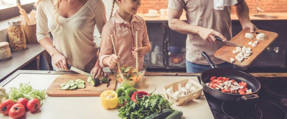 Girl and her parents are smiling while cooking at home in kitchen