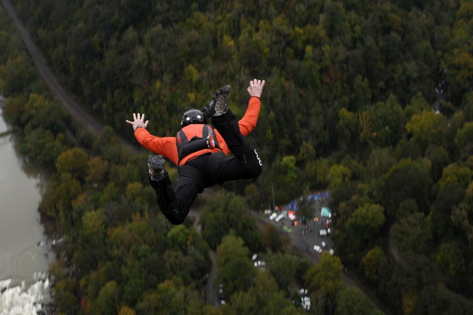 TOPSHOT - A daredevil with a pilot chute in his backpack plunges toward the New River after diving off the New River Gorge bridge on October 20, 2018 in Fayetteville, West Virginia. - 324 BASE jumpers -- people who parachute from fixed structures like bridges, skyscrapers,or cliffs -- participated in Bridge Day, which began in 1980 and has grown into one of the largest legal BASE jumping events in the world. (Photo by Michael Mathes / AFP) (Photo by MICHAEL MATHES/AFP via Getty Images)