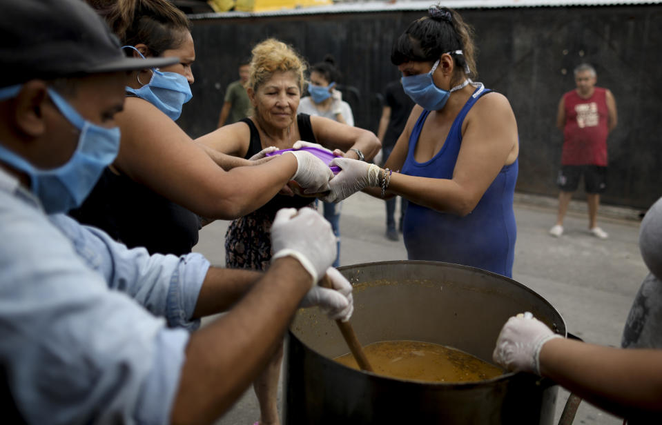 Alejandra Gómez, en el centro a la derecha, entrega un recipiente de plástico lleno de guiso de lentejas afuera de un comedor popular en las afueras de Buenos Aires, Argentina, el miércoles 25 de marzo de 2020. (AP Foto / Natacha Pisarenko)