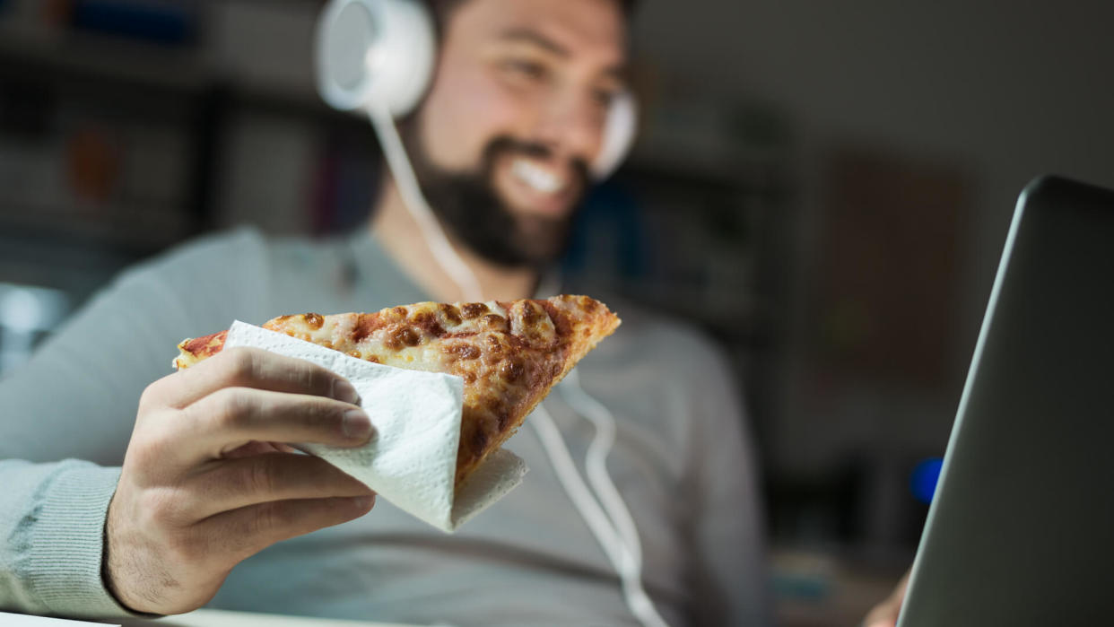 man eating pizza with headphones on computer