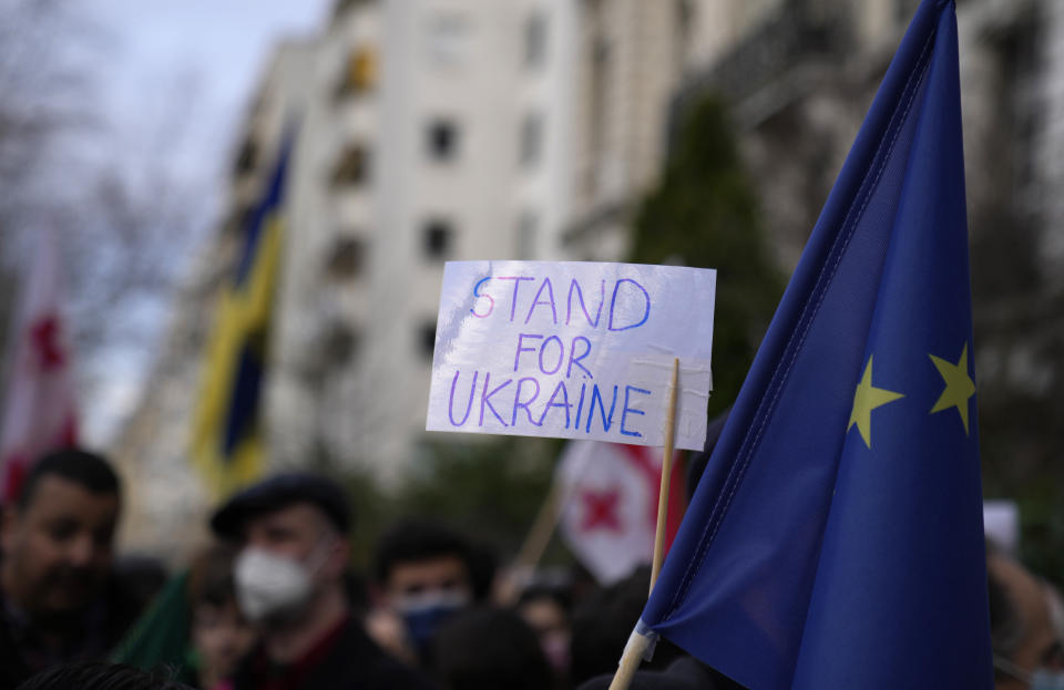 A protestor holds up a sign next to an EU flag during a demonstration in front of the Russian embassy in Paris, France, Tuesday, Feb. 22, 2022. World leaders are getting over the shock of Russian President Vladimir Putin ordering his forces into separatist regions of Ukraine and they are focusing on producing as forceful a reaction as possible. Germany made the first big move Tuesday and took steps to halt the process of certifying the Nord Stream 2 gas pipeline from Russia. (AP Photo/Francois Mori)