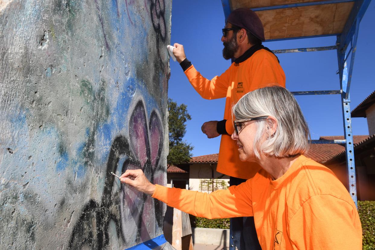 Carolyn MacLeod and Nick Seraphim, of KC Restoration, use solvents Monday, Nov. 6, 2023, to clean the surface of the Berlin Wall as they prepare for the restoration of its artwork at The Ronald Reagan Presidential Library & Museum in Simi Valley.