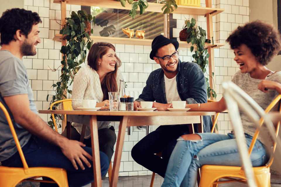 Group of four friends, two men and two women, laughing and enjoying coffee together at a cafe table