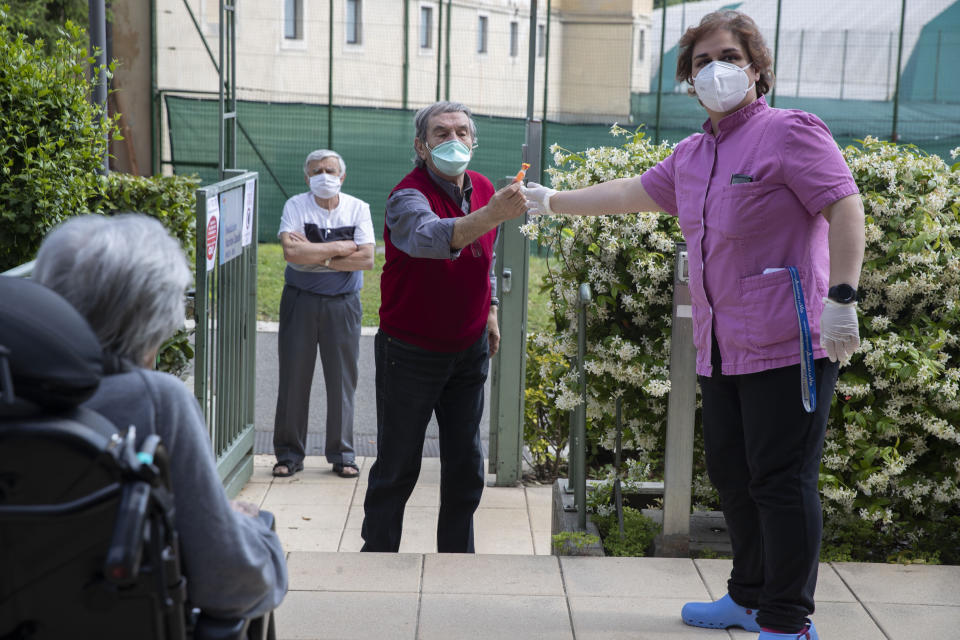 Tommaso Tondini gives a candy to Melania Cavalieri, to be handed to his wife Anita Perico as she sits in her wheelchair from a safe distance at the Martino Zanchi Foundation nursing home in Alzano Lombardo, Italy, Friday, May 29, 2020. Loved ones are being allowed to reunite with residents of the Martino Zanchi Foundation nursing home in the northern Italian town of Alzano. It comes after more than three months of separation and worry amid the coronavirus pandemic. Alzano, close to Bergamo, is the site of one of Italy's biggest outbreaks, centered around the town's hospital. (AP Photo/Luca Bruno)