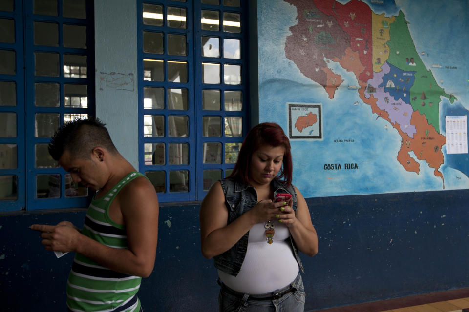 People check their phones as they waits to vote at Republica de la Argentina school in San Jose, Costa Rica, Sunday, Feb. 2, 2014. Presidential elections in two Central American countries Sunday are both referendums on political stagnation, with voters in Costa Rica deciding whether to oust the long-ruling party, and voters in El Salvador deciding whether to bring it back to power. (AP Photo/Moises Castillo)