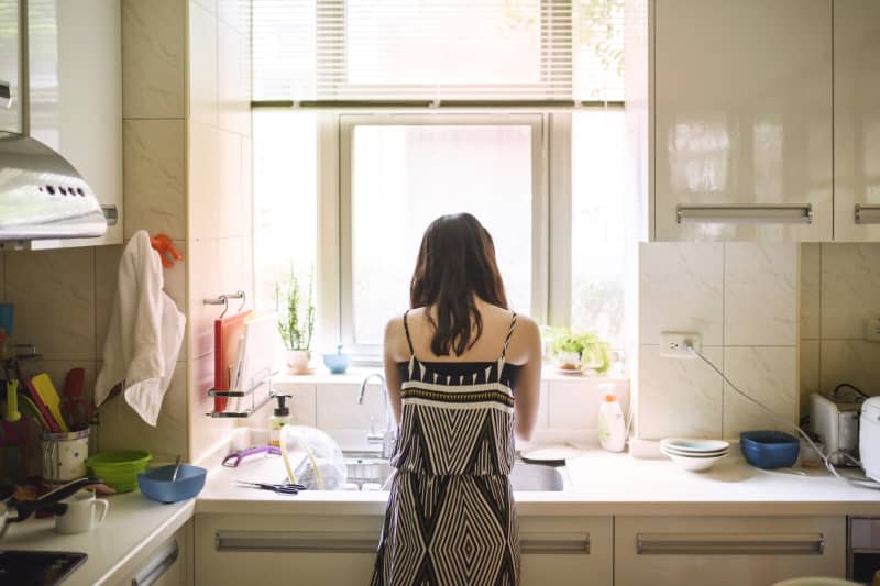 Rear view of woman at kitchen sink in front of window doing dishes