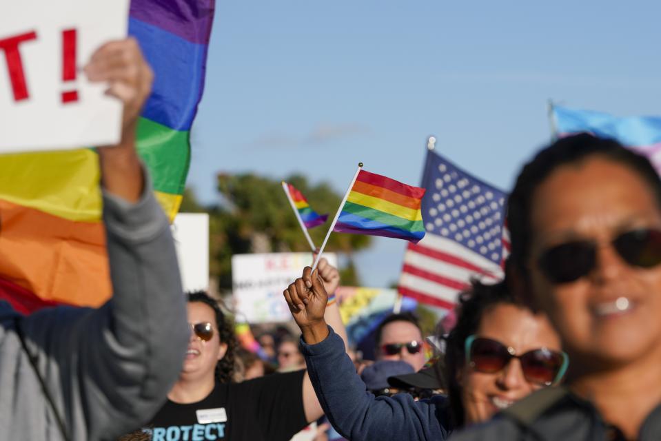 FILE - Marchers wave U.S. and rainbow flags and signs as they walk at the St. Pete Pier in St. Petersburg, Fla., on Saturday, March 12, 2022 during a rally and march to protest the controversial "Don't say gay" bill passed by Florida's Republican-led legislature and now on its way to Gov. Ron DeSantis' desk. Florida's state government and LGBTQ+ advocates have settled a lawsuit challenging a law that bars teaching about sexual orientation and gender identity in public schools. (Martha Asencio-Rhine/Tampa Bay Times via AP, File)