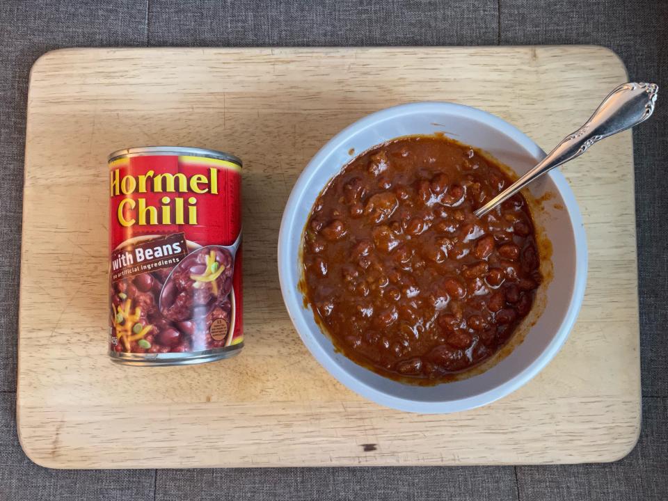 Can of Homel chili beside a white bowl of chili