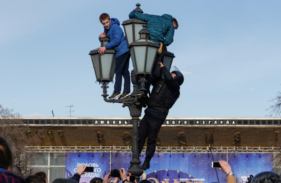 A law enforcement officer climbs a lamp pole to detain opposition supporters in Moscow.