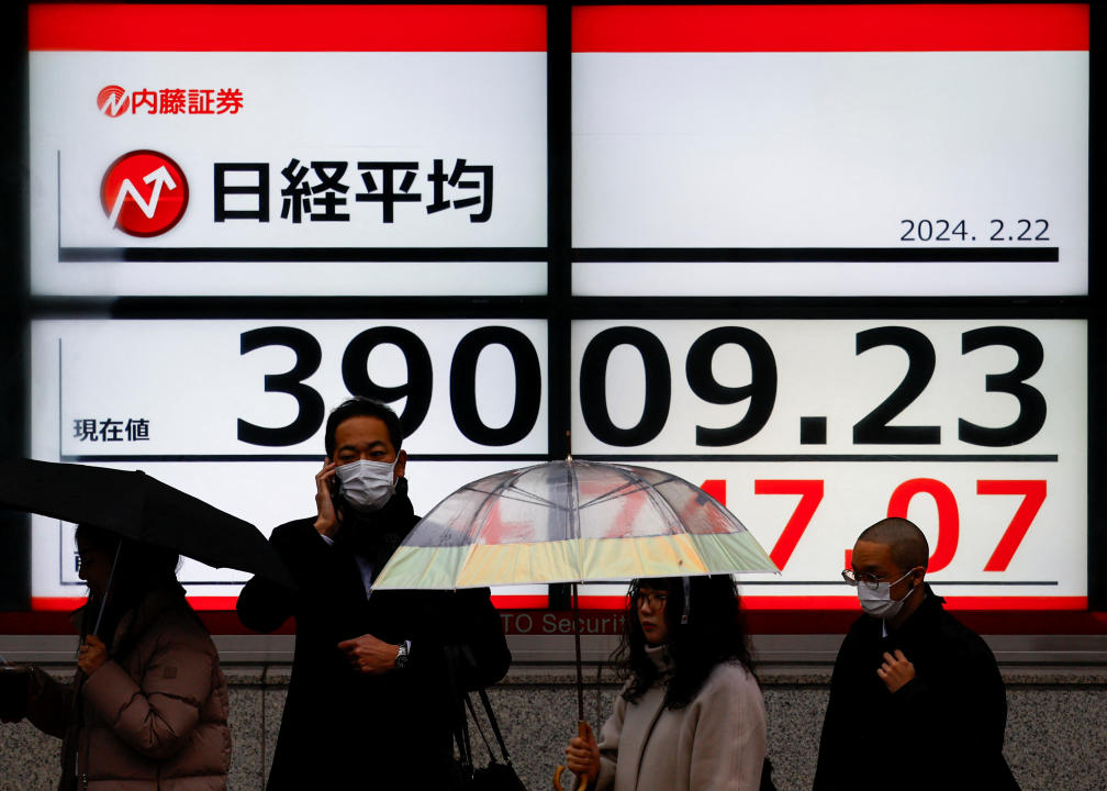 Passersby stand in front of electronic screens displaying Japan's Nikkei share average, which surged past an all-time record high scaled in December 1989, outside a brokerage in Tokyo, Japan February 22, 2024. REUTERS/Issei Kato