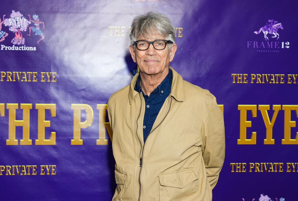 Eric Roberts stands against a purple backdrop with logos and text reading "The Private Eye." He is wearing glasses, a tan jacket, and a blue shirt