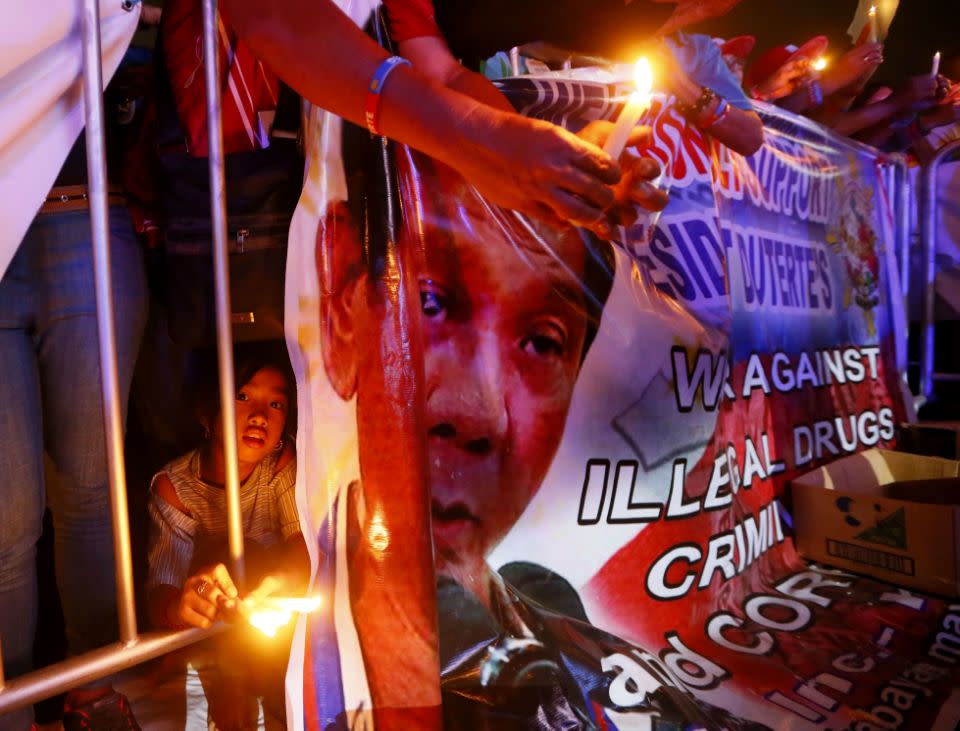 A girl holds a lighted candle beside a tarpaulin showing Mr Duterte during an overnight vigil in Manila in support for the war on drugs. Photo: EPA