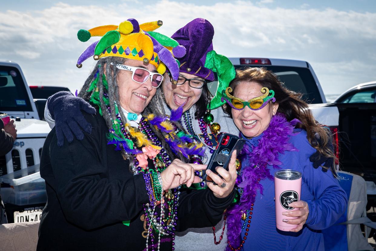 From left, Susan Wilson, Alma Silman, and Linda Calhoun, look at selfies they took before the Barefoot Mardi Gras Parade on North Padre Island, Saturday, Feb. 18, 2023, in Corpus Christi, Texas.