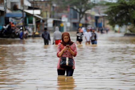 A woman uses her mobile phone while walking in flood waters after heavy seasonal rains caused the Citarum river to flood in Dayeuhkolot, south of Bandung, West Java province, Indonesia, February 23, 2018. REUTERS/Darren Whiteside