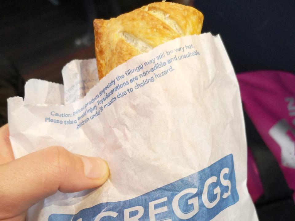 bag of Greggs sausage roll wit someone holding it