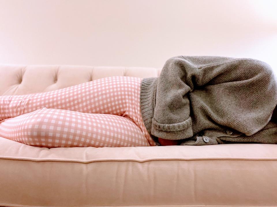 mid adult woman clutches stomach while lying down on couch