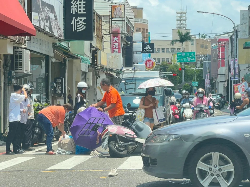 機車後座女乘客慘摔，暖心路人幫忙撐傘，還灑水降溫。民眾提供