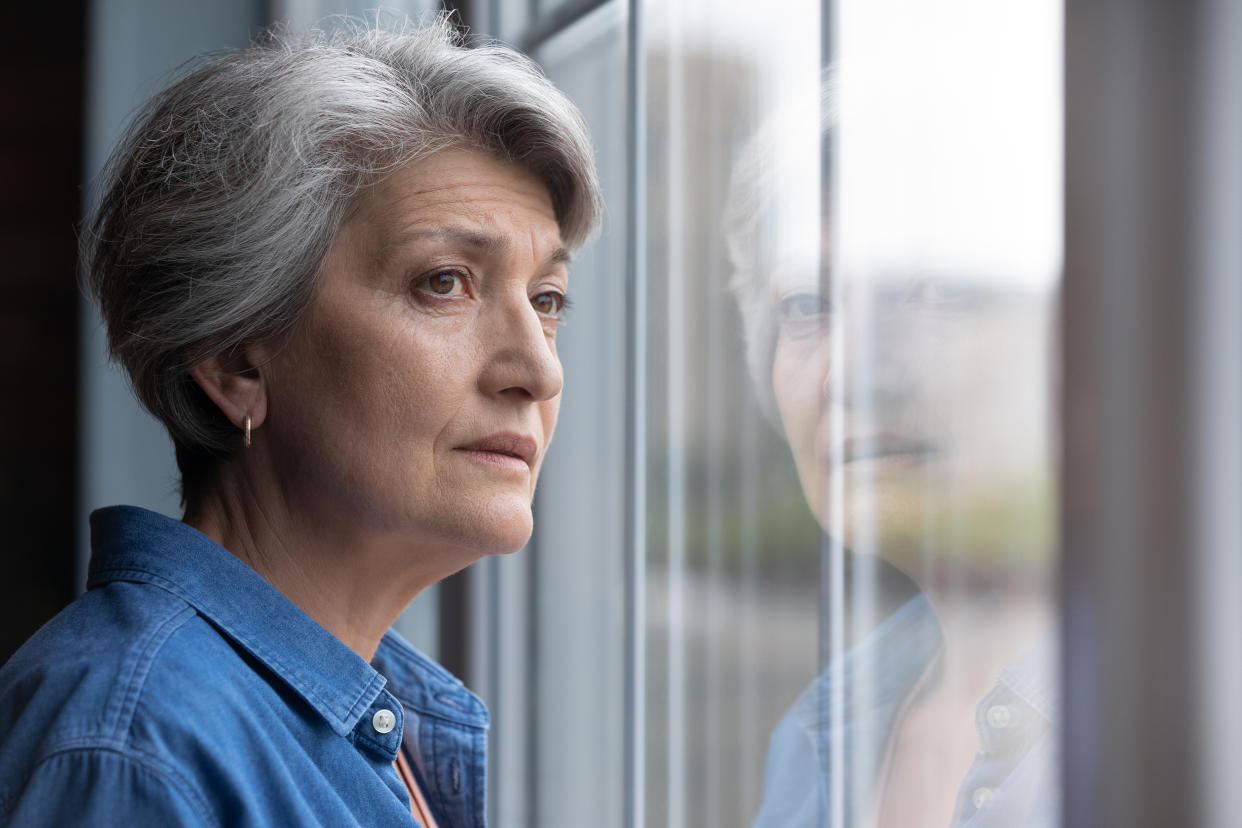 Lonely elderly Caucasian 60s woman look in window distance mourning or yearning at home. Sad mature grey-haired female lost in thoughts feel lonely abandoned in retirement house. Solitude concept. (Getty Images)