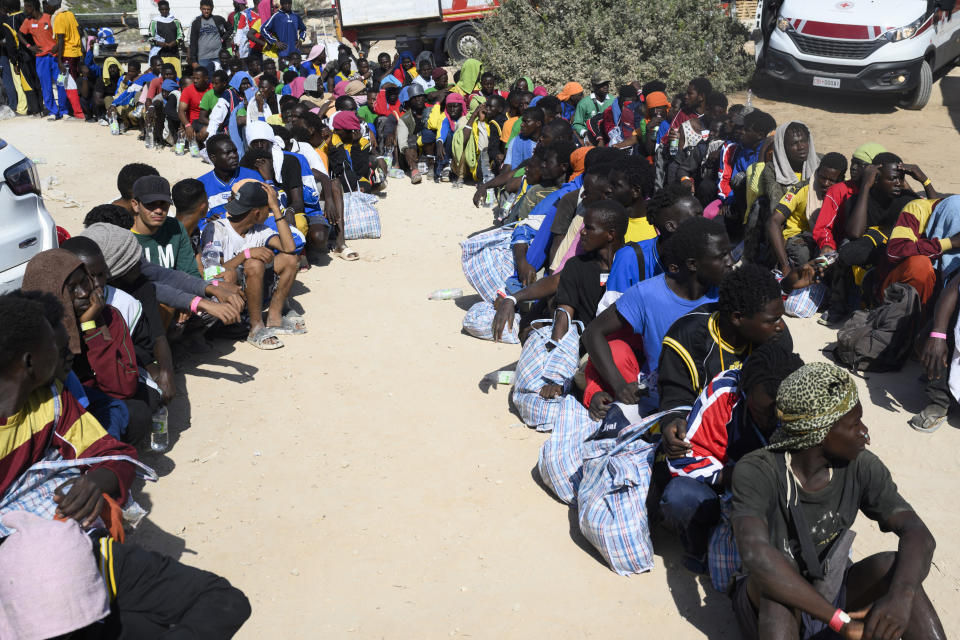 FILE - Migrants sit outside the Lampedusa's migrant reception center, Sicily, Thursday, Sept.14, 2023. Thousands of migrants and refugees have landed on the Italian island of Lampedusa this week after crossing the Mediterranean Sea on small unseaworthy boats from Tunisia, overwhelming local authorities and aid organizations . (AP Photo/Valeria Ferraro, File)