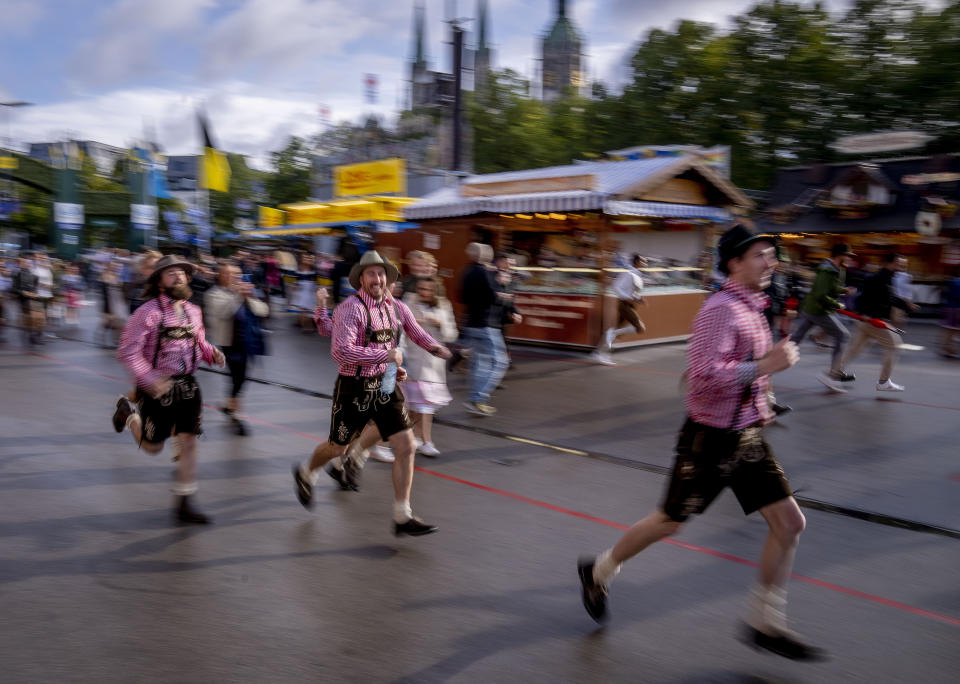 Visitors run onto the festival ground on the opening day of the 187th Oktoberfest beer festival in Munich, Germany, Saturday, Sept. 17, 2022. Oktoberfest is back in Germany after two years of pandemic cancellation, the same bicep-challenging beer mugs, fat-dripping pork knuckles, pretzels the size of dinner plates, men in leather shorts and women in cleavage-baring traditional dresses. (AP Photo/Michael Probst)