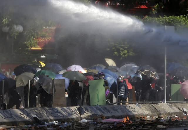 Protesters shelter with umbrellas as an armoured police vehicle sprays them with water