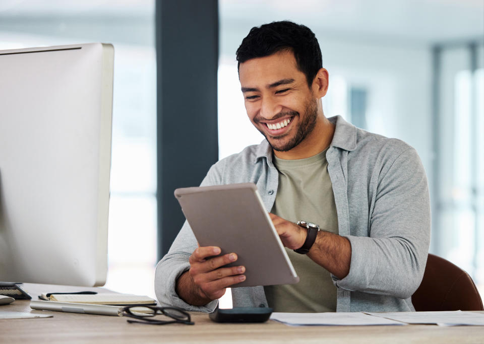 Man using tablet in front of desktop computer, smiling. 
