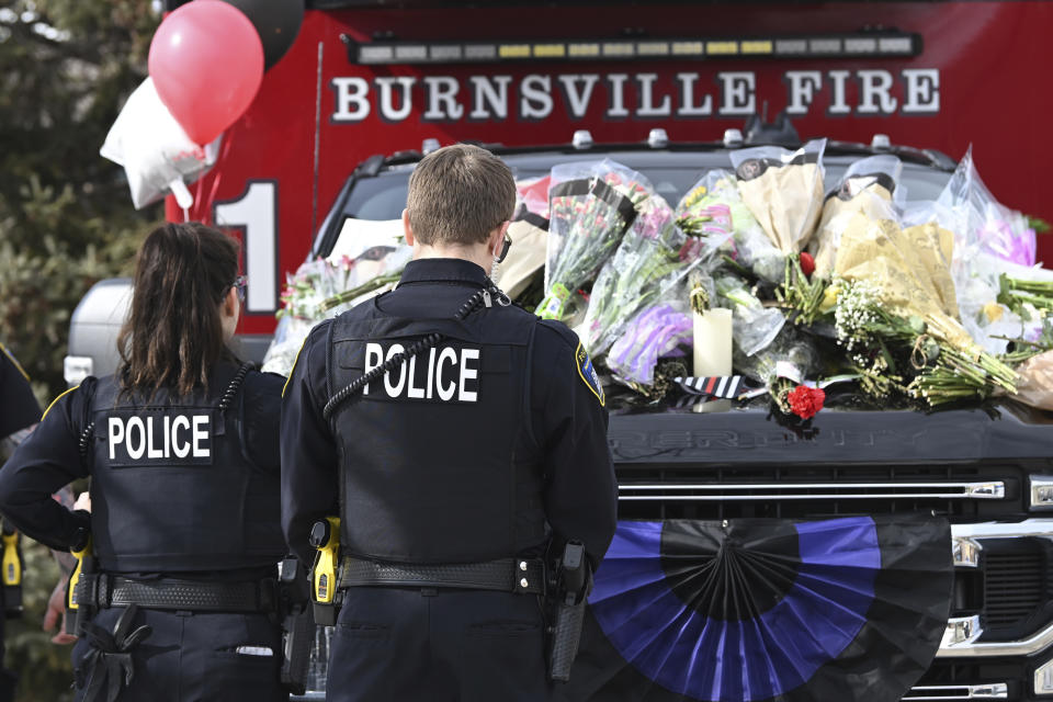 Eden Prairie police officers pause next to memorials in front of the Burnsville Police Department in Burnsville, Minn., Monday, Feb. 19, 2024. Two police officers and a firefighter who responded to a domestic situation at a suburban Minneapolis home were killed early Sunday during a standoff by a heavily armed man who shot at police from the home where seven children were also inside. (Craig Lassig/Pioneer Press via AP)