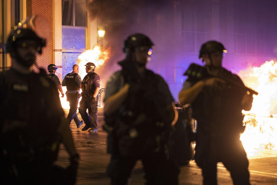 Police stand guard after protesters set fire to dumpsters after a vigil was held for Winston Boogie Smith Jr. early on Saturday, June 5, 2021. Authorities say Smith, wanted on a weapons violation, fired a gun from inside his vehicle before he was fatally shot by members of a federal task force as they were trying to arrest him. (AP Photo/Christian Monterrosa)