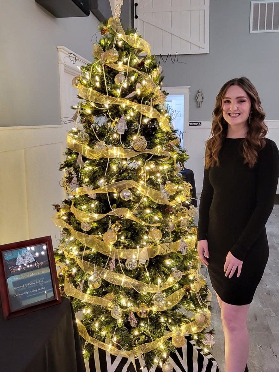 Marketing intern Audrey Walker poses in front of the Purdue Federal Credit Union tree she decorated for the 2022 Festival of Trees Gala.