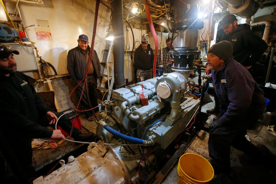 Pedro Cura, owner of the fishing boat Fisherman, looks on as the crew of Windward Power Systems installs the wiring for the new engine, they are installing in the hull of the New Bedford fishing boat.