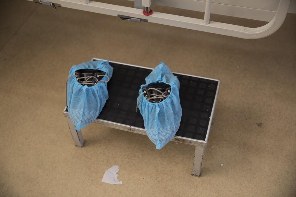 A patient's shoes enveloped in shoe covers sit on a stool beside his bed inside the intensive care unit for people infected with the new coronavirus, at the 2 de Mayo Hospital, in Lima, Peru, Friday, April 17, 2020. (AP Photo/Rodrigo Abd)