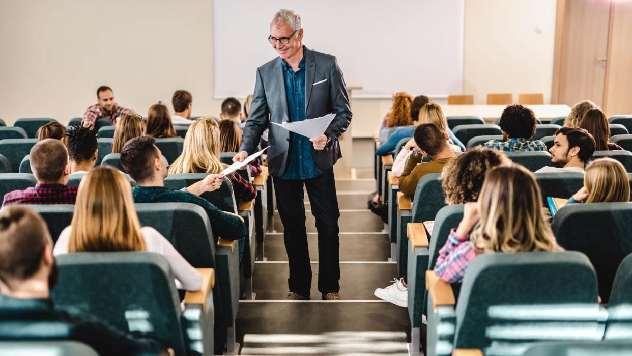 Happy senior professor talking to his students while giving them test results in lecture hall.