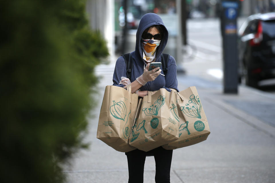 NEW YORK NY, - APRIL 12: A woman with groceries looks at her portable telephone while wearing protective gloves and a homemade mask amid the coronavirus pandemic on April 12, 2020 in New York City. COVID-19 has spread to most countries around the world, claiming over 114,000 lives with infections at over 1.8 million people. (Photo by John Lamparski/Getty Images)