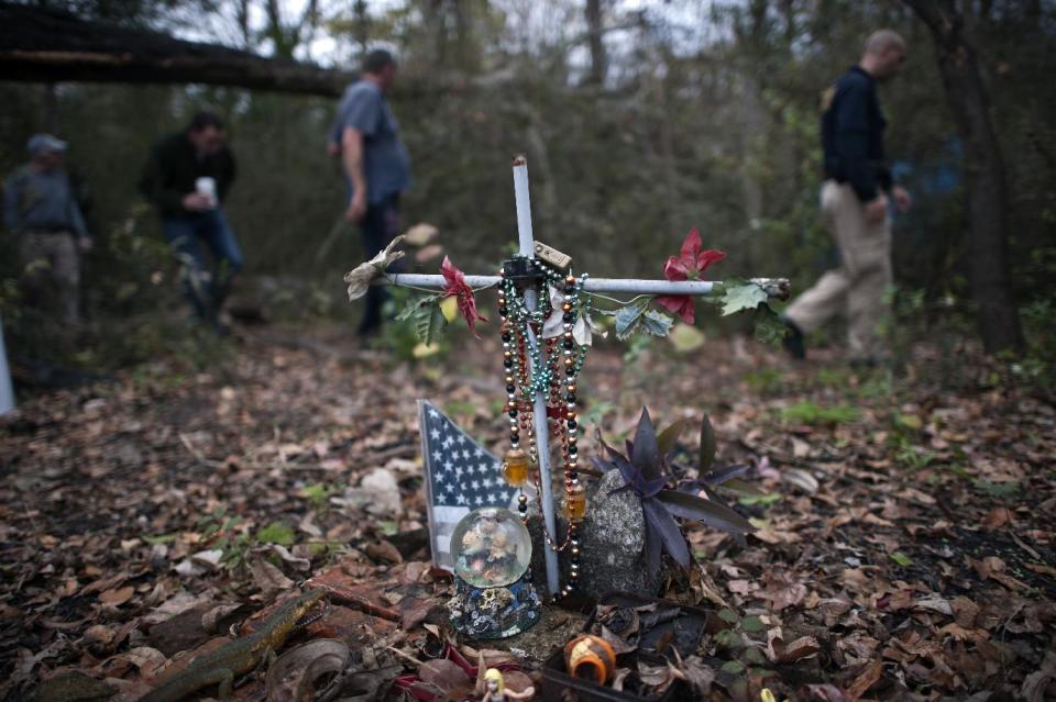 In this Saturday, Dec. 14, 2013 photo, Homeless Liaison Officer Tom Gentner, right, leads a group wanting to donate clothing past a memorial for a woman who died in a tent fire in Camp 2 in a wooded area behind the Savannah College of Art and Design's Boundary Village in Savannah, Ga. The tent ignited from the sparks of a nearby campfire. (AP Photo/Stephen B. Morton)