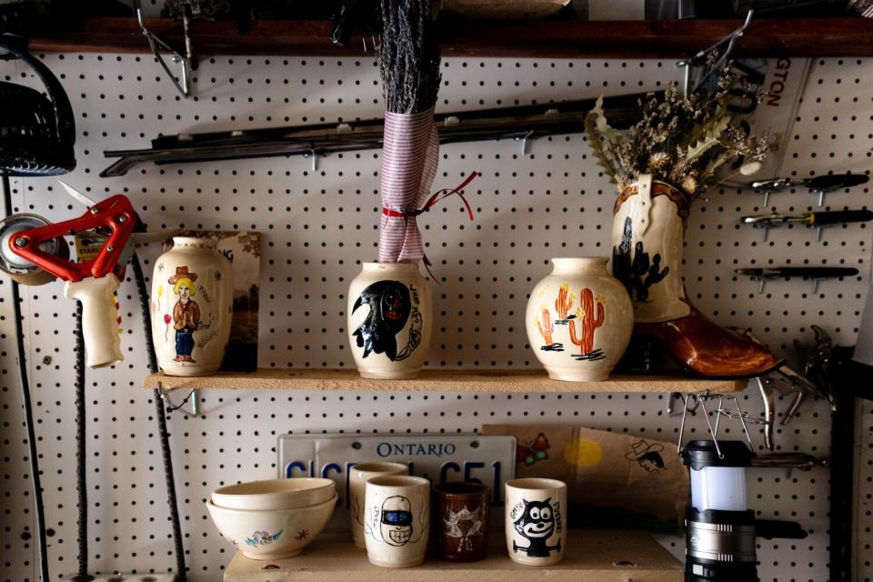 Ceramic vases, tumblers and bowls on shelves in front of a pegboard wall