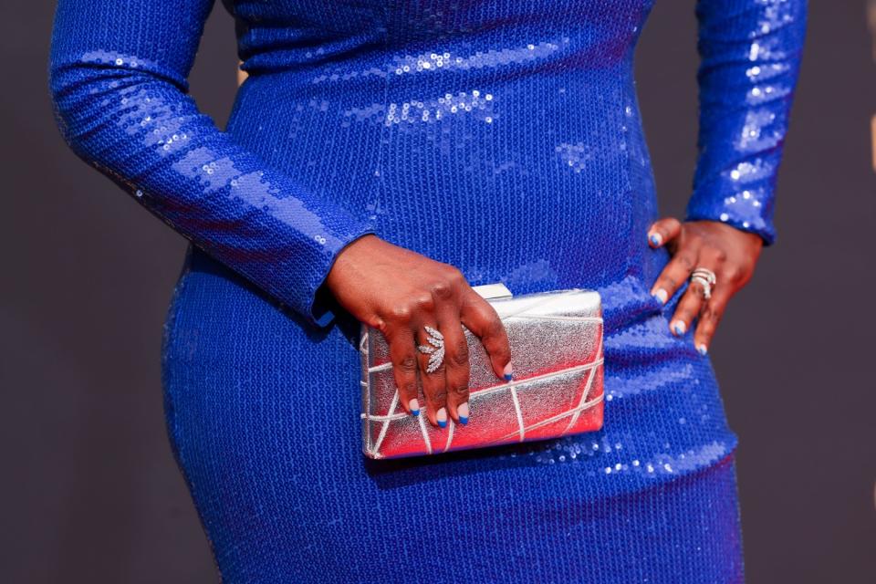 The abdomen and arms of a woman holding a silver clutch purse against her bright blue gown.