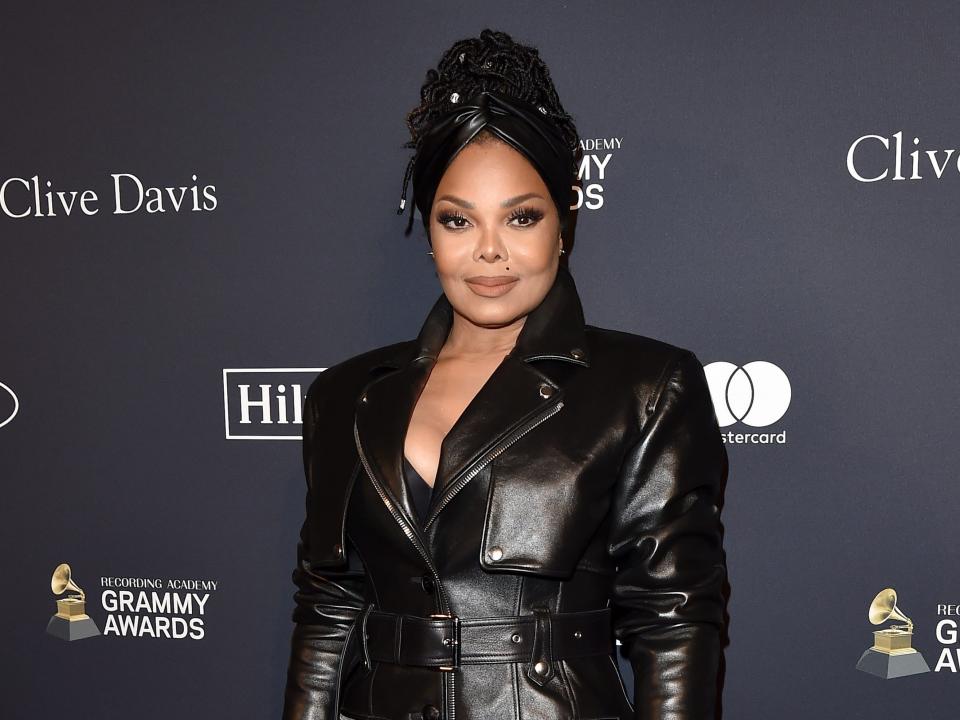 Janet Jackson with an updo and black trench coat on a red carpet.