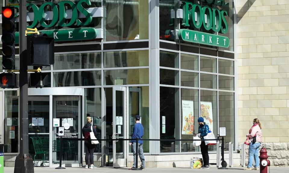 Shoppers wait in line at a Whole Foods grocery store in Minneapolis, Minnesota, 21 March 2020.