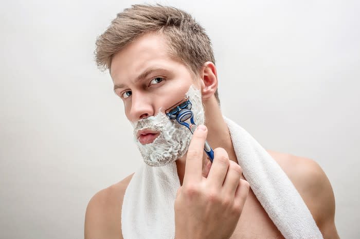 Man shaving with white towel around neck.