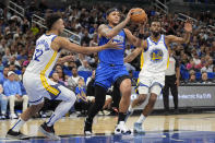 Orlando Magic forward Paolo Banchero, center, passes the ball as he gets between Golden State Warriors forward Trayce Jackson-Davis (32) and forward Andrew Wiggins (22) during the first half of an NBA basketball game Wednesday, March 27, 2024, in Orlando, Fla. (AP Photo/John Raoux)