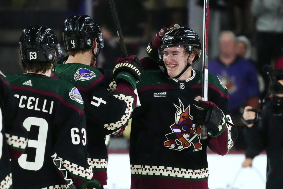 Arizona Coyotes' Josh Doan, right, smiles as he celebrates his two-goal NHL debut with Juuso Valimaki (4) and Matias Maccelli (63), after the team's hockey game against the Columbus Blue Jackets on Tuesday, March 26, 2024, in Tempe, Ariz. The Coyotes won 6-2. (AP Photo/Ross D. Franklin)