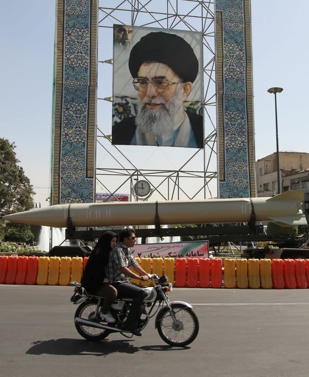 An Iranian motorcyclist drives past a Shahab-2 missile that is displayed in front of a large portrait of Ayatollah Ali Khamenei in a square south of Tehran, on September 23, 2012