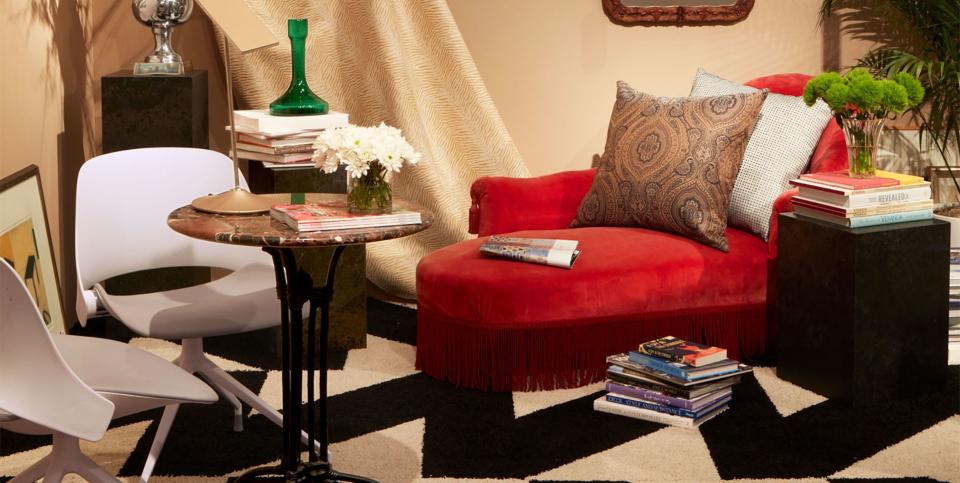 room with black and white zigzag rug and a fringed red velvet chaise a big drape from ceiling and a small pedestal table with modern white chairs