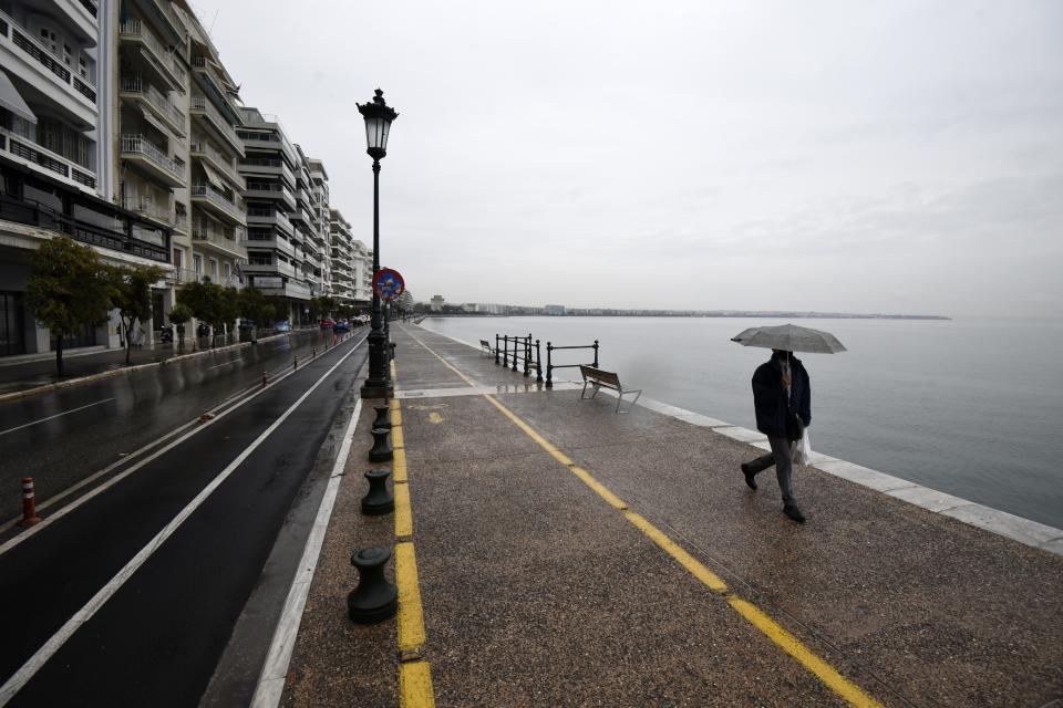 A pedestrian holds an umbrella as he walks on a coastal avenue during the lockdown to contain the spread of COVID-19 in the northern city of Thessaloniki, Greece, Tuesday, Nov. 3, 2020. Greece's government imposed a localized lockdown on its second largest city of Thessaloniki and the northern province of Serres, after major increases in the number of coronavirus infections there. (AP Photo/Giannis Papanikos)