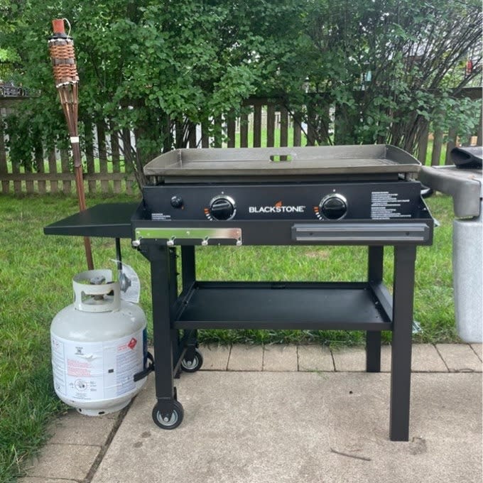 Blackstone gas grill on a lawn with left side shelf extended and propane tank attached