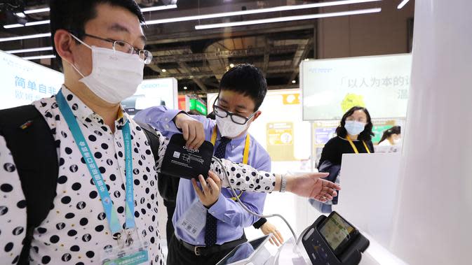 Seorang pengunjung (pertama dari kiri) mencoba alat pengukur tekanan darah di stan Omron di area ekshibisi Peralatan dalam Pameran Impor Internasional China (China International Import Expo/CIIE) ketiga di Shanghai, China timur, pada 5 November 2020. (Xinhua/Fang Zhe)